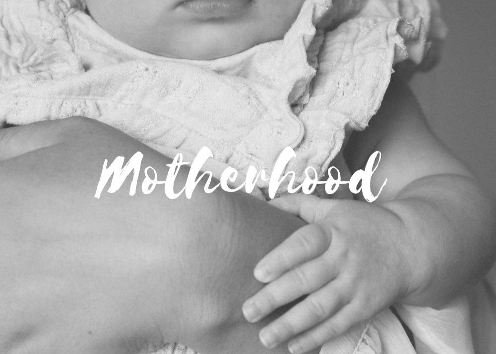 Black and white photo of a baby holding onto a person with the word 'Motherhood' overlaid.