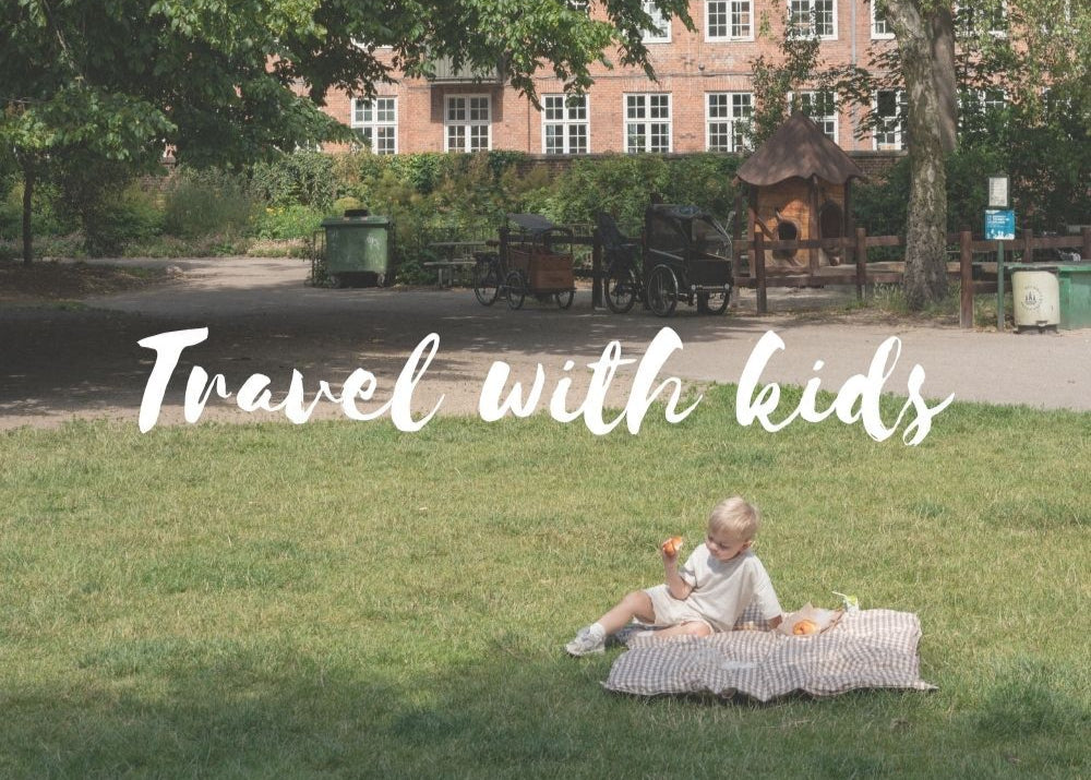 Child sitting on a blanket in a park with text 'Travel with kids' overlayed.