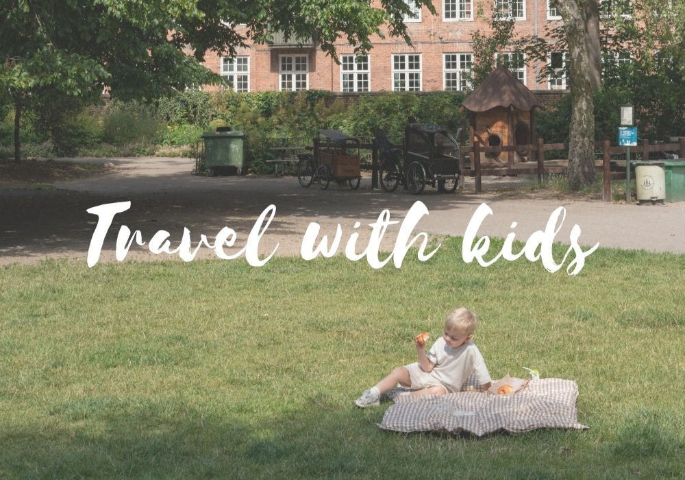 Child sitting on a blanket in a park with text 'Travel with kids' overlayed.