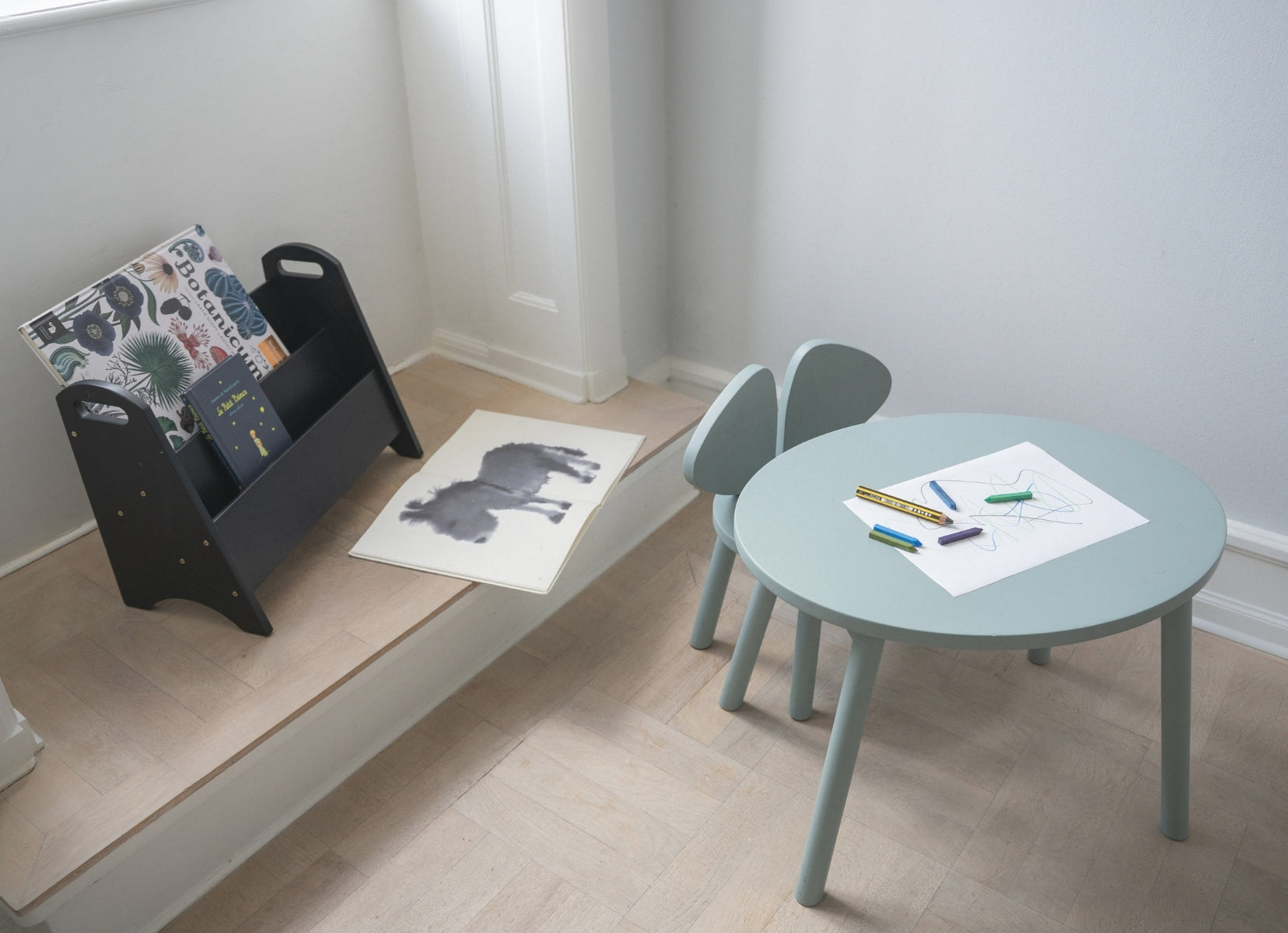 Children's table and chairs with art supplies on a light wood floor.