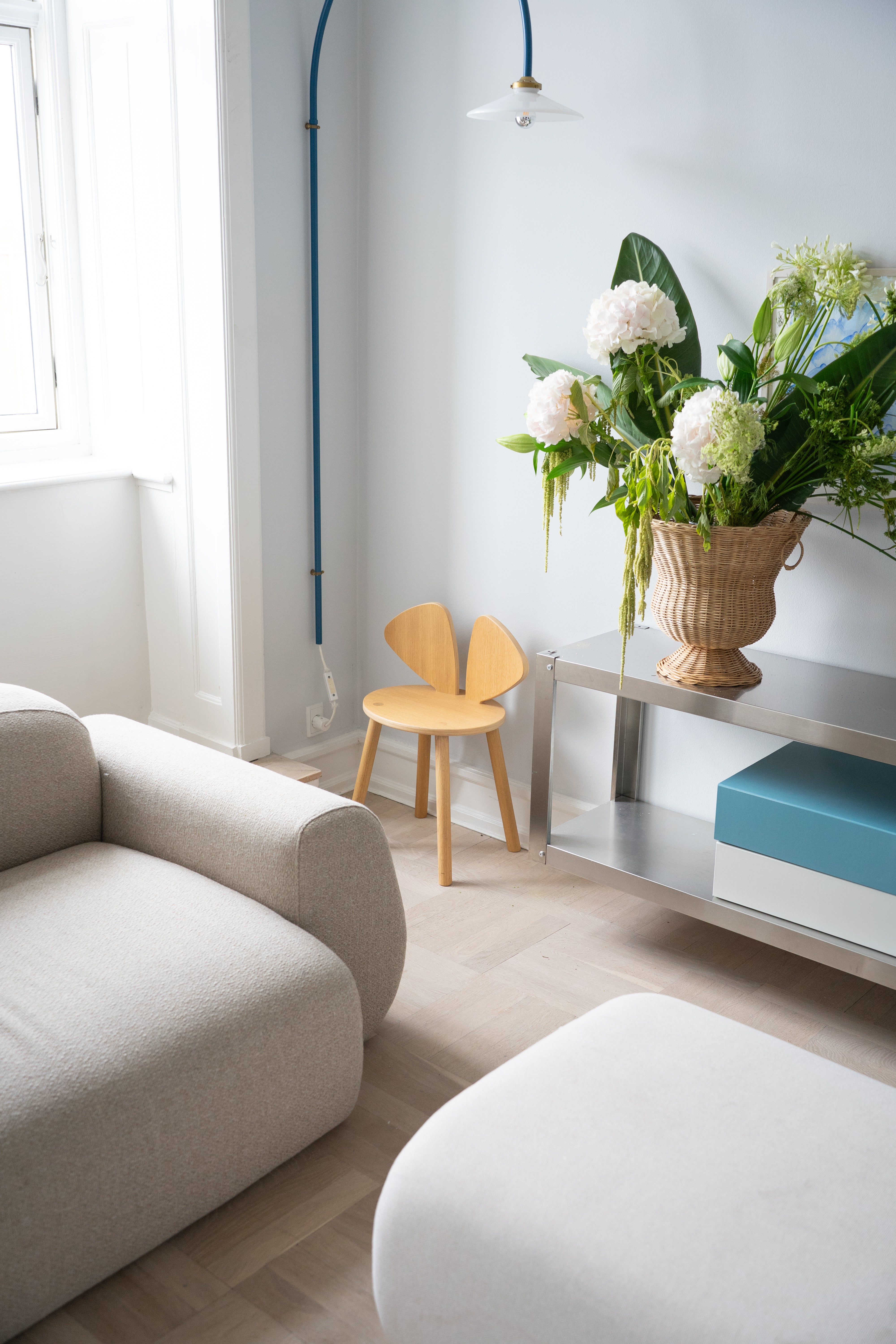 Modern living room with a beige sofa, wooden chair, and a vase of flowers on a shelf.