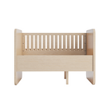 A light natural wood baby crib or toddler bed frame with vertical slats on the back panel, shown from the front on a plain white background.