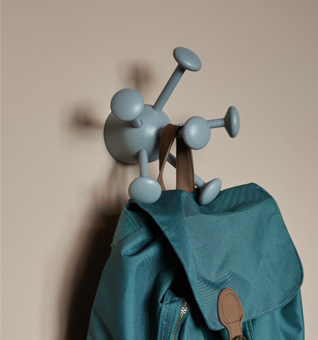 Blue wall hook with a green backpack on a beige background
