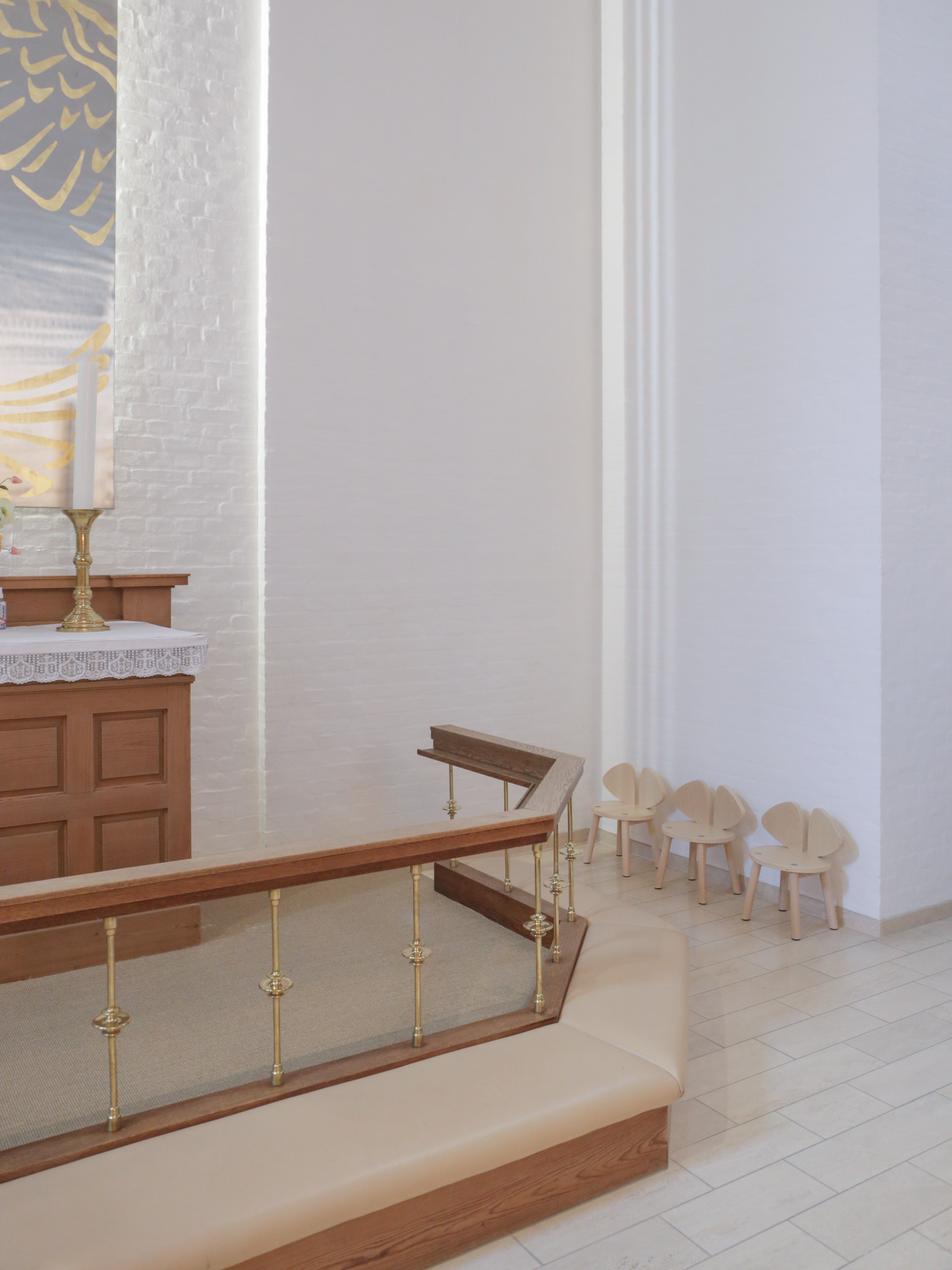 Interior of a building with wooden benches and chairs against a white wall.