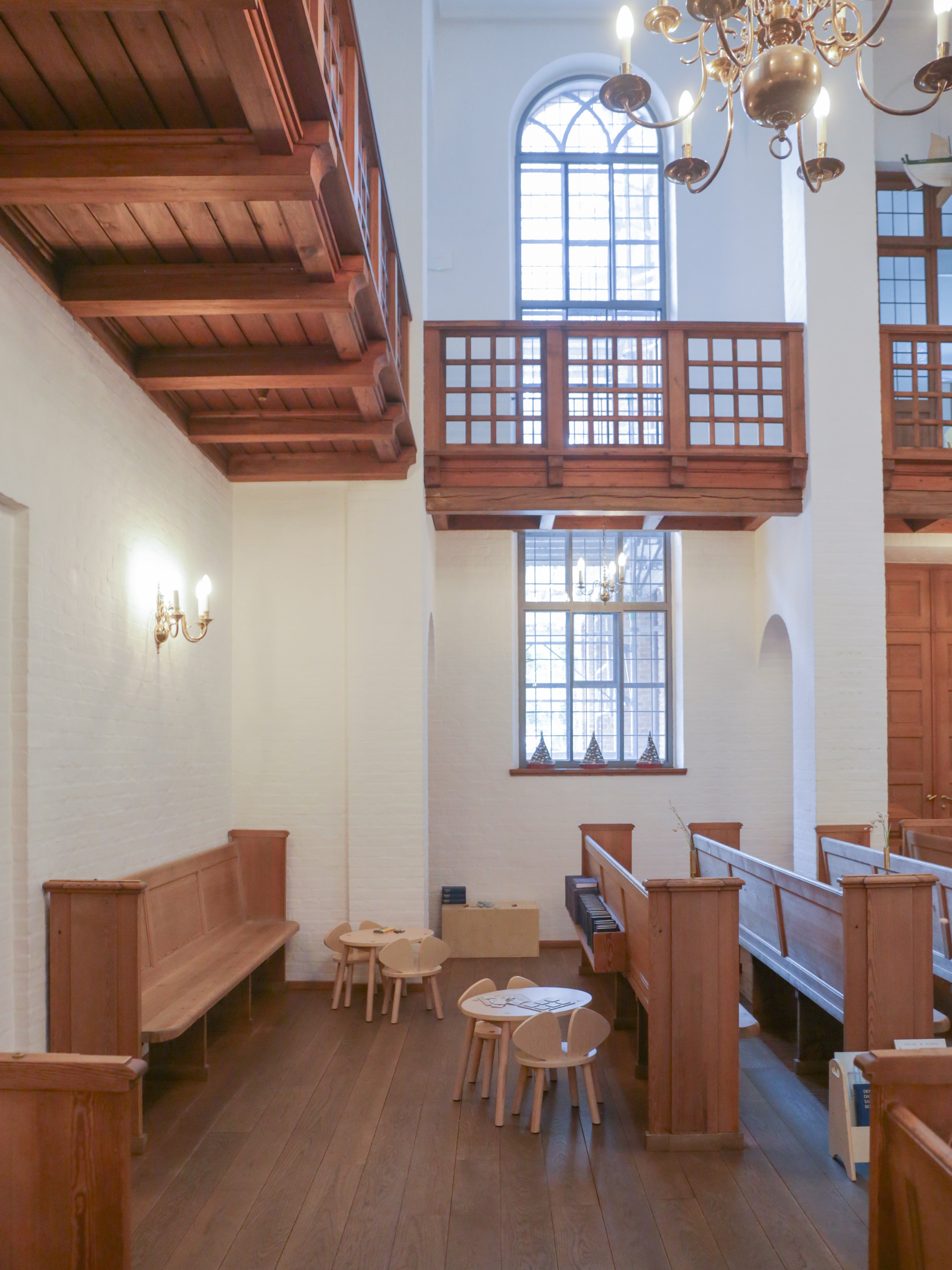Interior of a church with wooden pews, tables, and chairs, high ceiling with wooden beams.