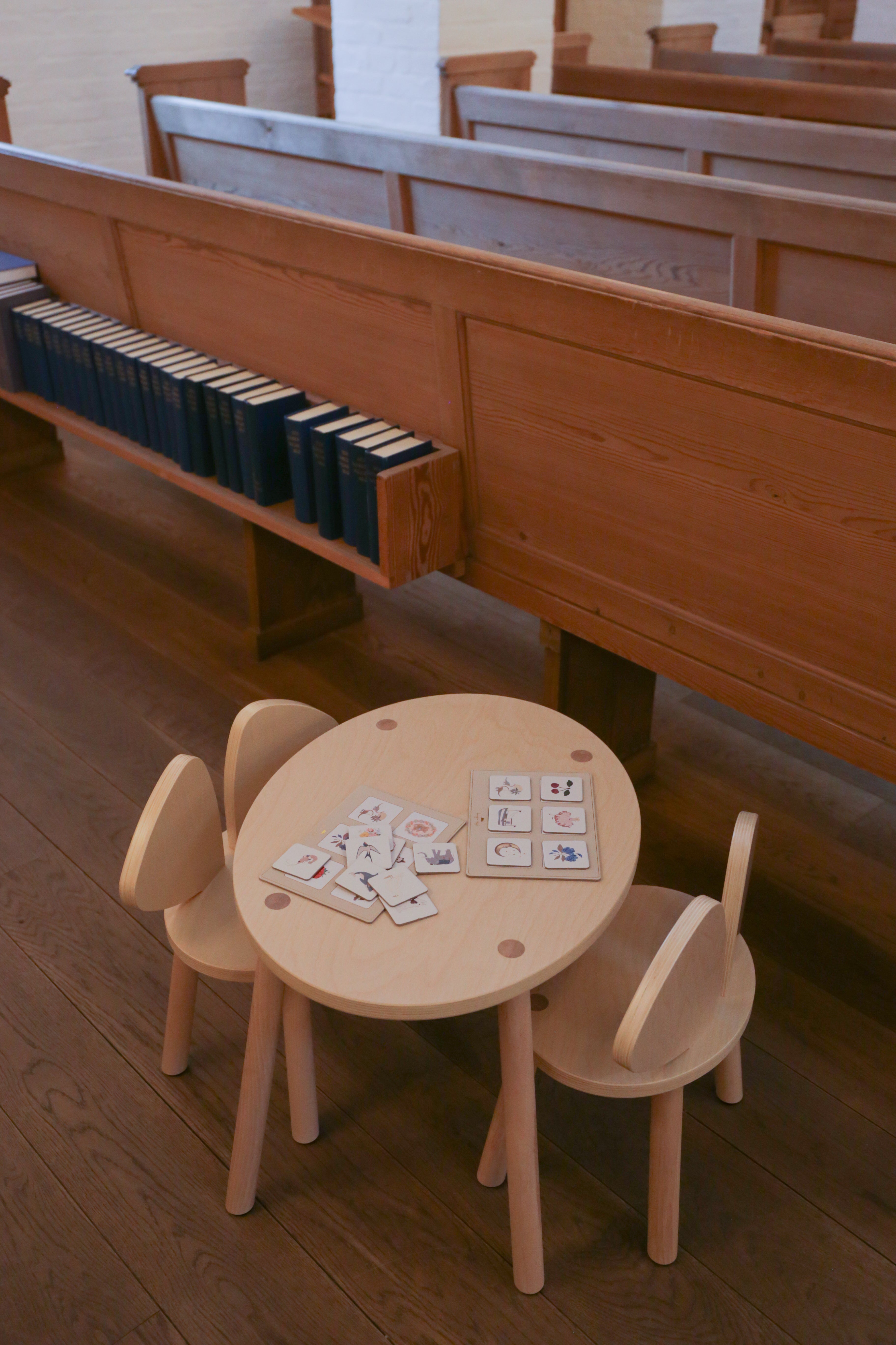 Wooden children's table and chairs with cards on a wooden floor, likely in a church setting.
