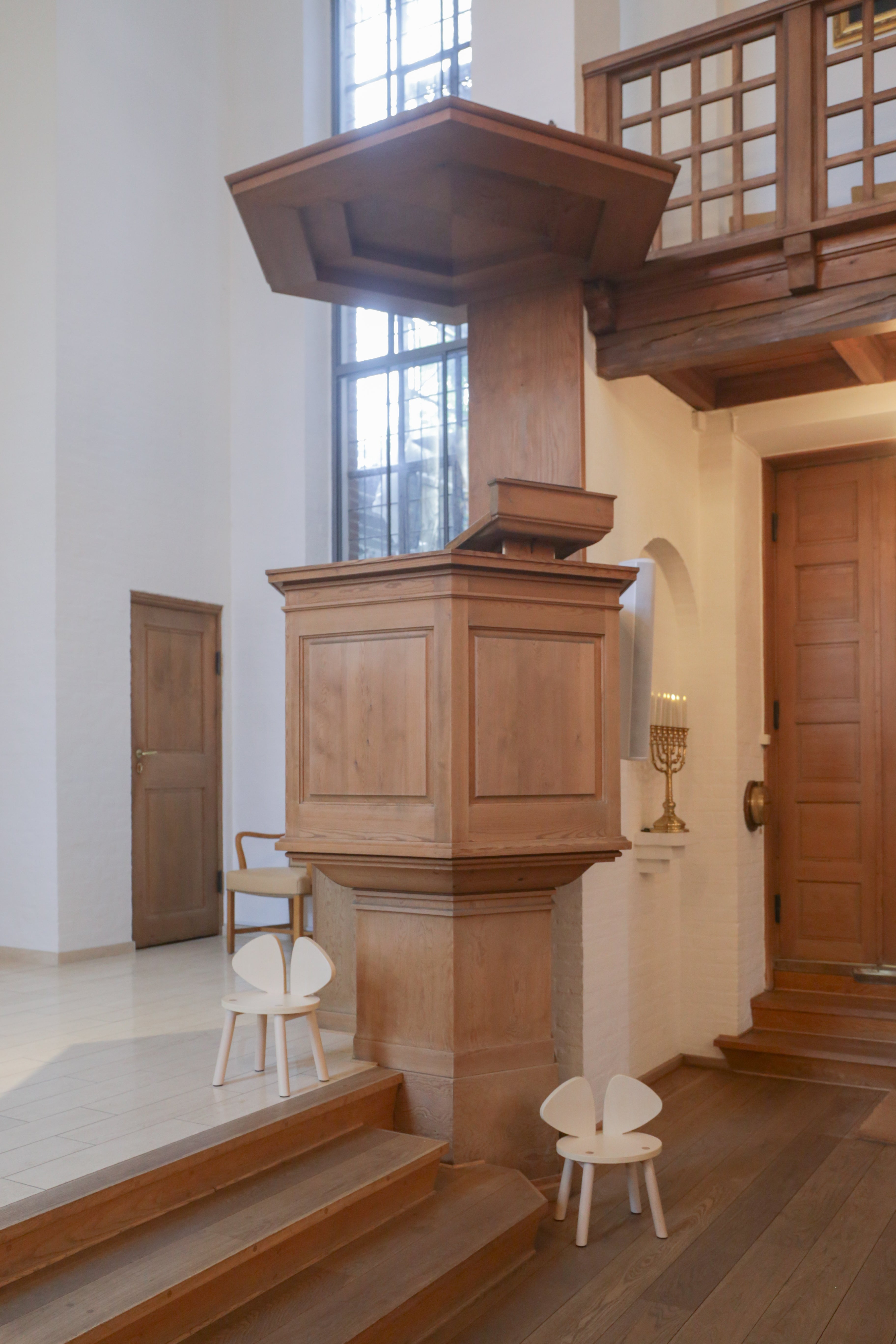 Wooden pulpit in a church setting with stained glass windows and wooden doors.