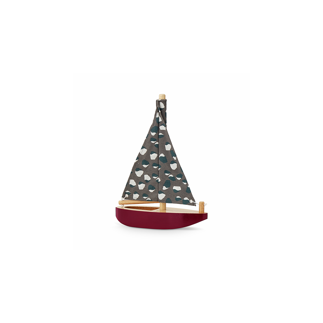 A small wooden toy sailboat with a dark gray patterned sail, teal and white motifs, and a deep red hull, shown on a plain white background.