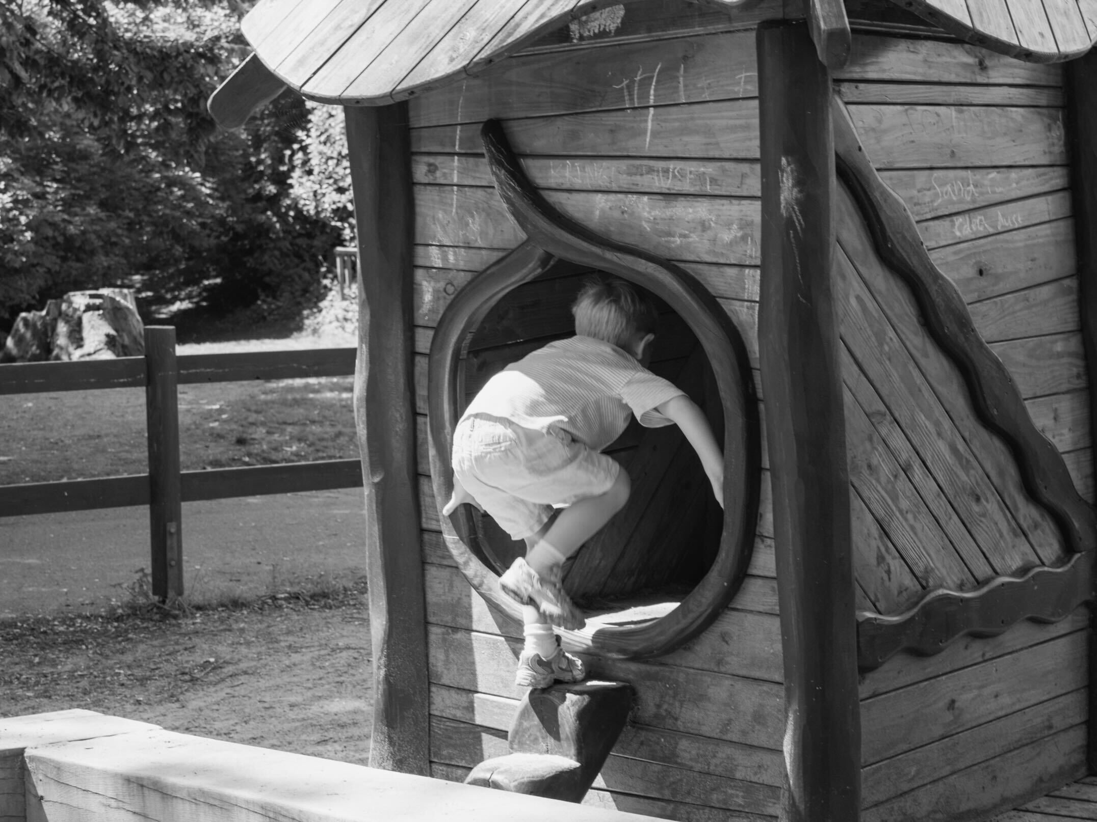 Child playing on a wooden playhouse with a circular door.