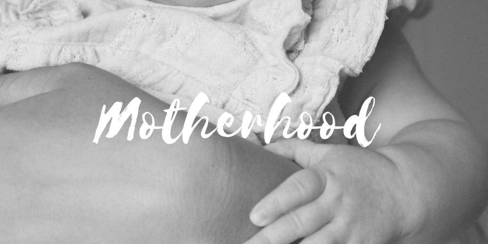 Black and white photo of a baby holding onto a person with the word 'Motherhood' overlaid.