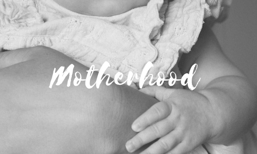 Black and white photo of a baby holding onto a person with the word 'Motherhood' overlaid.