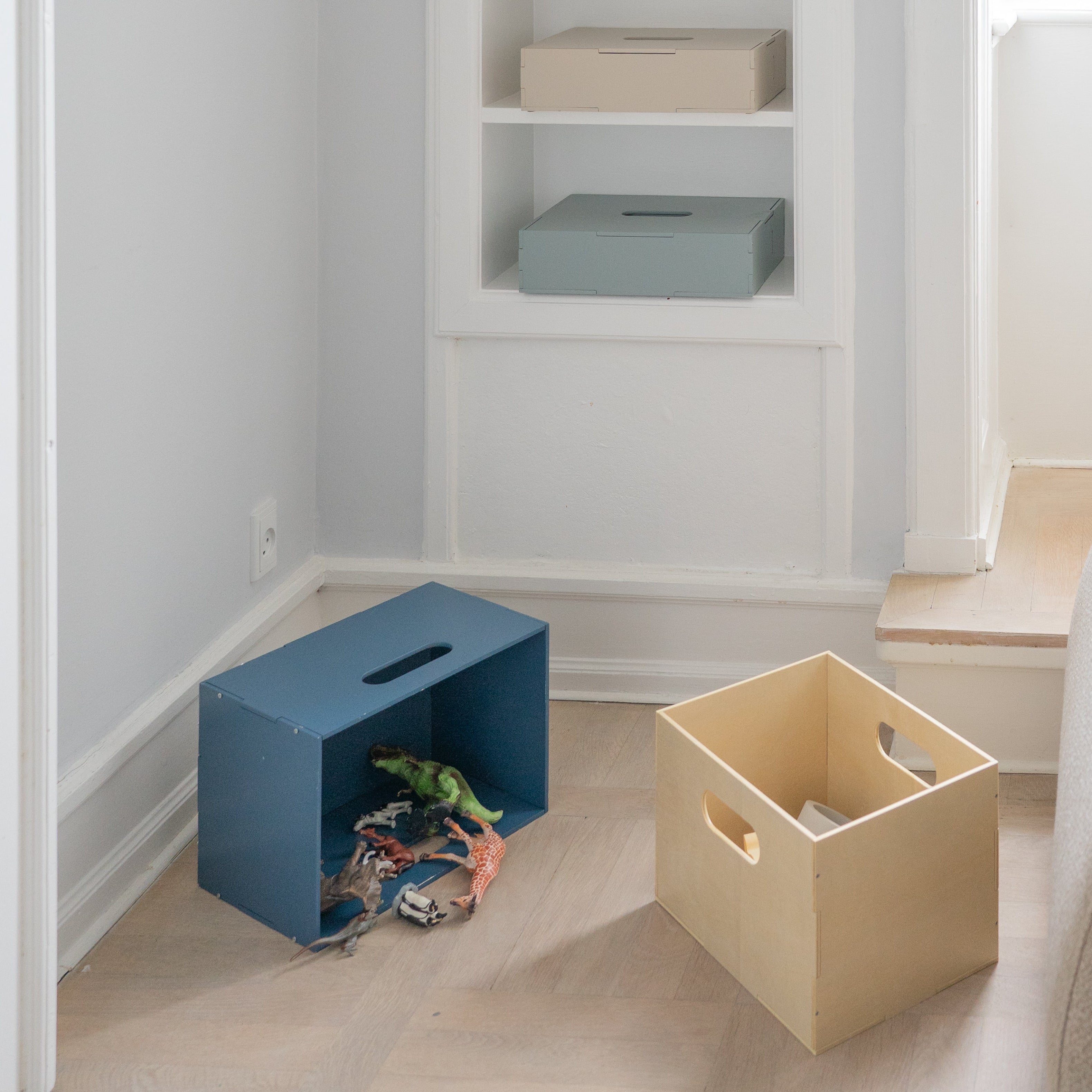 Children's room with a bookshelf, storage boxes, and toys on a light wooden floor.