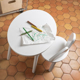 White children's table and chair set on a terracotta tiled floor with drawing materials.