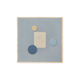 A square abstract wall art piece with a light blue linen-like center, a natural wood frame, a beige rectangular block, and three circular shapes in beige wood, dark blue, and light blue, shown on a white background.