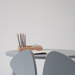 A minimalist light gray children's table and chair set with a small wooden pencil holder on the table, set against a plain light gray wall.
