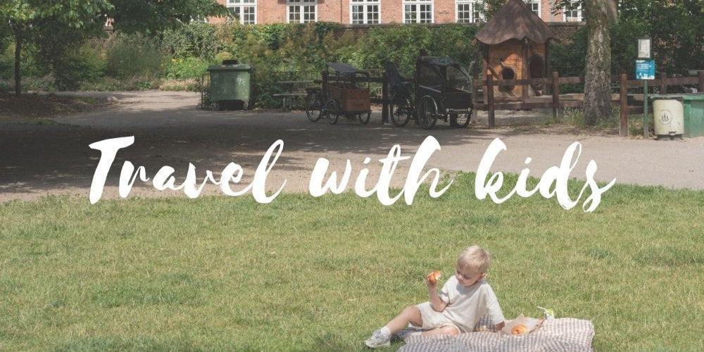 Child sitting on a blanket in a park with text 'Travel with kids' overlayed.