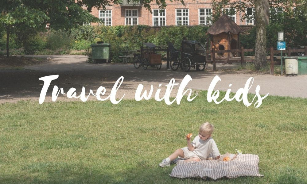 Child sitting on a blanket in a park with text 'Travel with kids' overlayed.