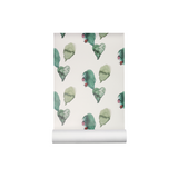 A roll of wallpaper with a repeating pattern of watercolor green leaves and small red berries on a warm off-white background, shown partially unrolled.