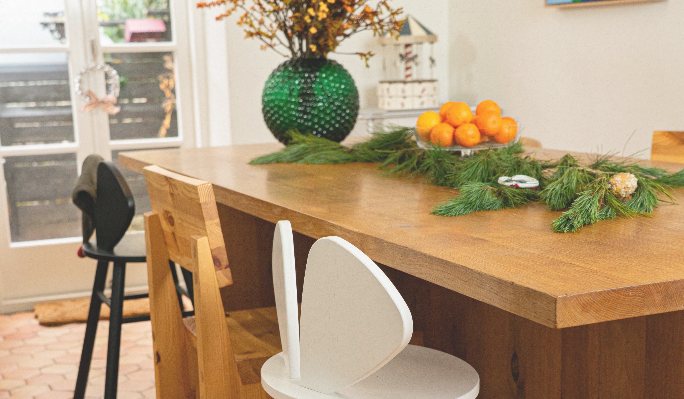 Dining table with greenery and oranges, surrounded by chairs in a bright room.