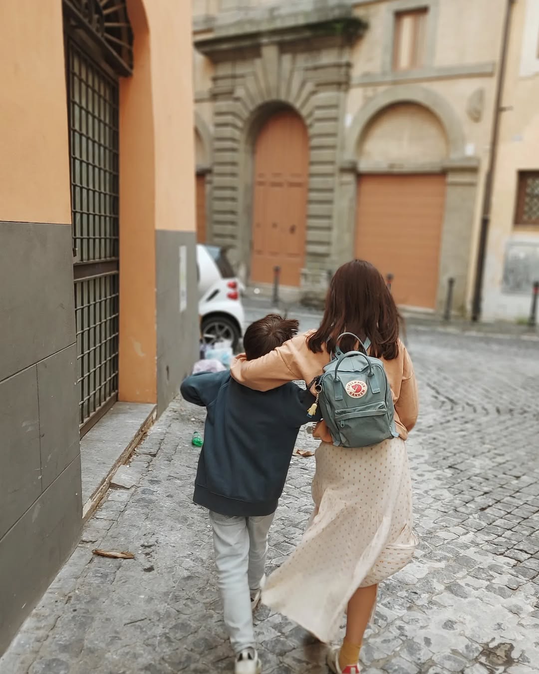 Two people walking down a cobblestone street with a building in the background
