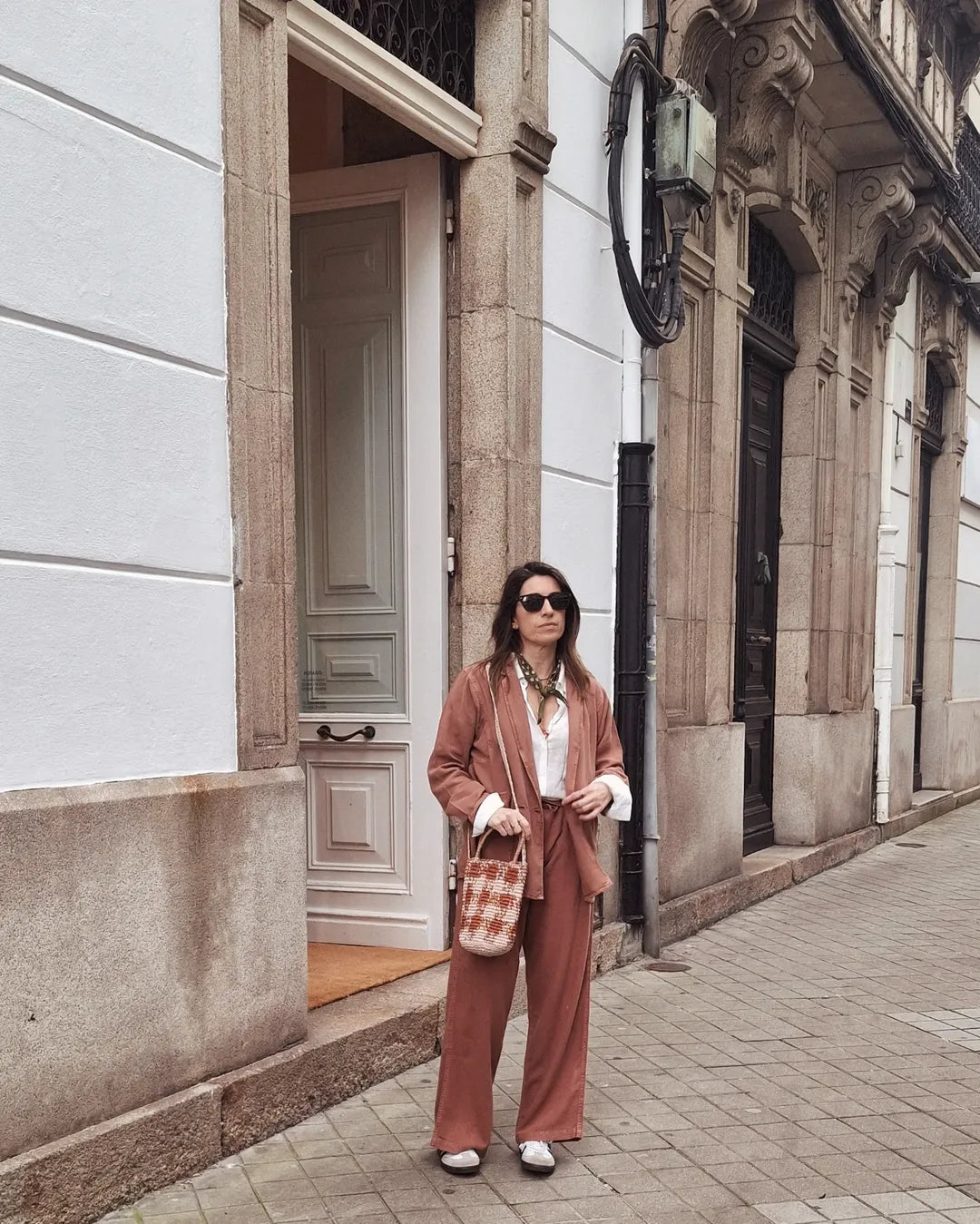 Woman in a pink suit standing on a city street with classical architecture.
