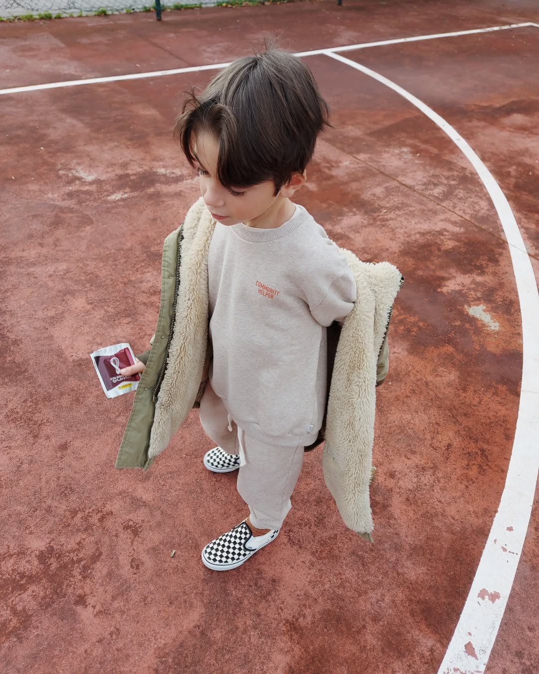Child standing on a basketball court holding a phone