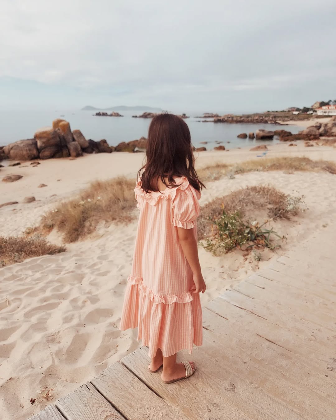 girl in a pink dress standing on a wooden boardwalk by the beach