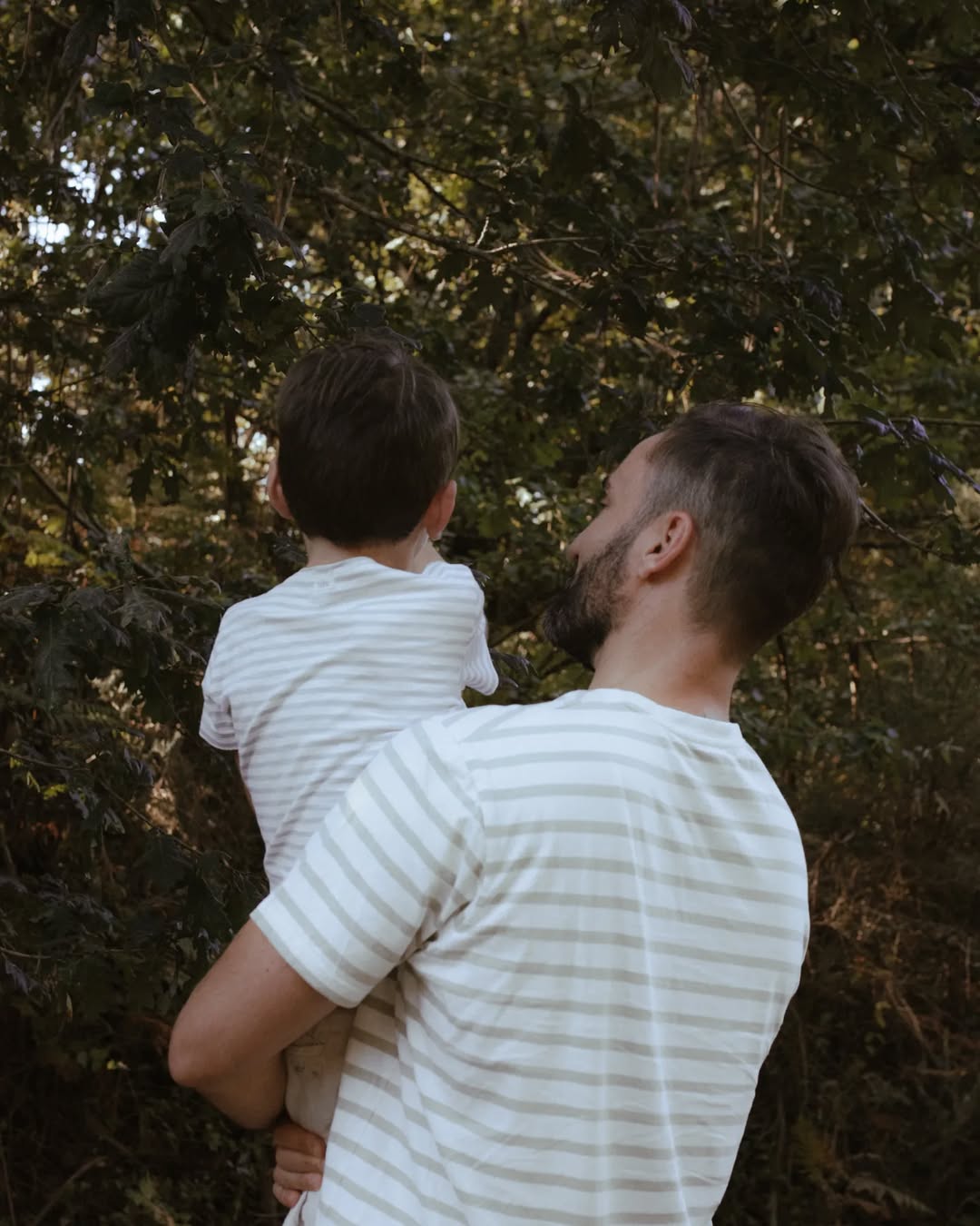 Man and child in striped shirts standing among trees