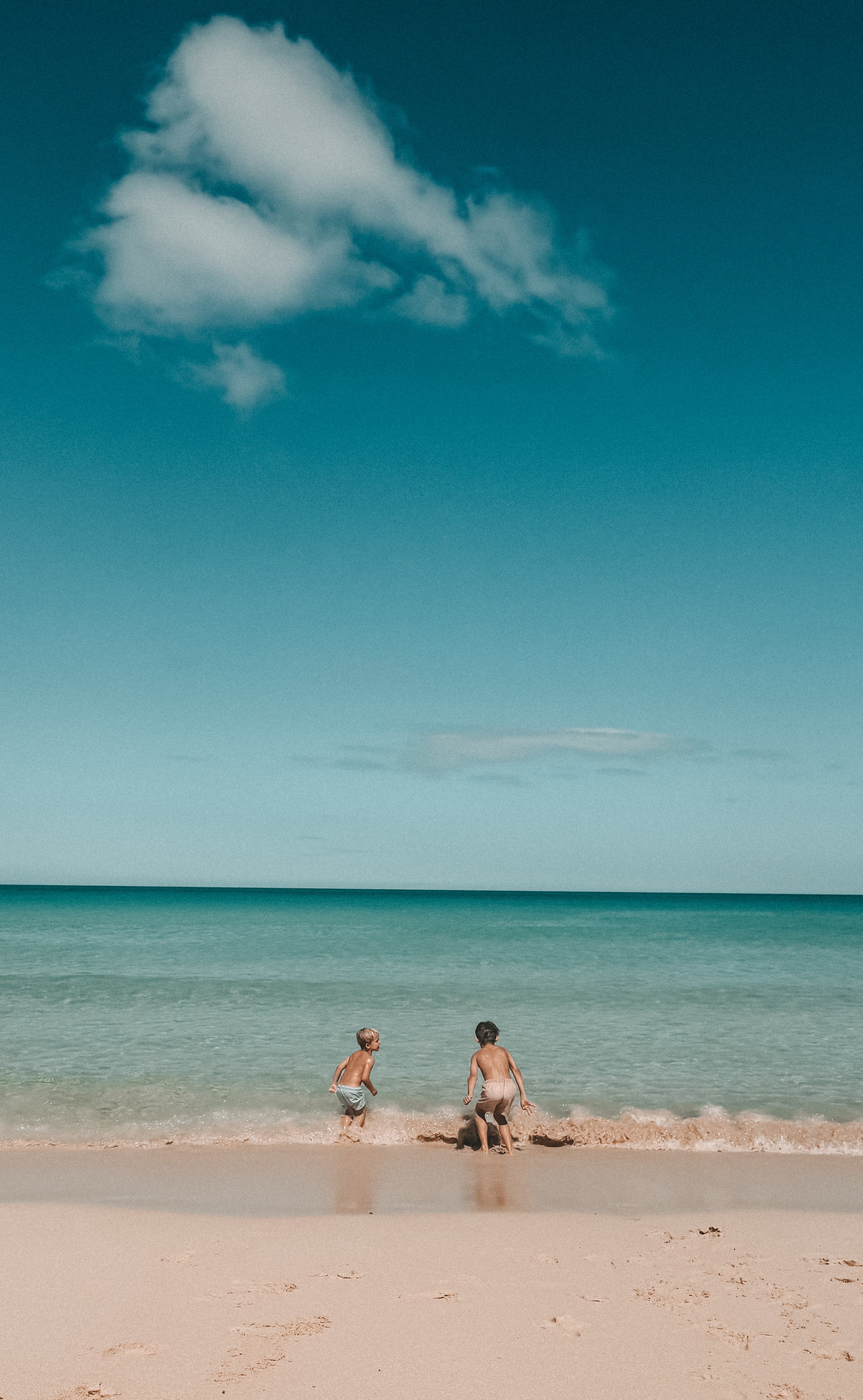 Two people standing on a beach with clear blue sky and ocean.