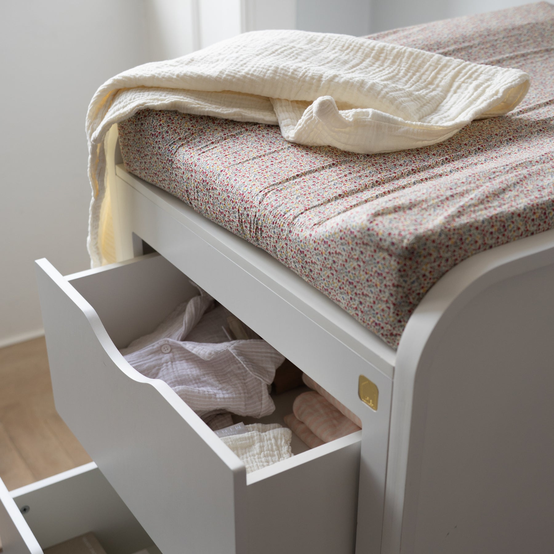 White bed with open drawer revealing clothes, against a light background