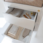 Open drawer with baby items including a seat cover, clothes, and a brush on a white background