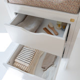 Open drawer with baby items including a seat cover, clothes, and a brush on a white background