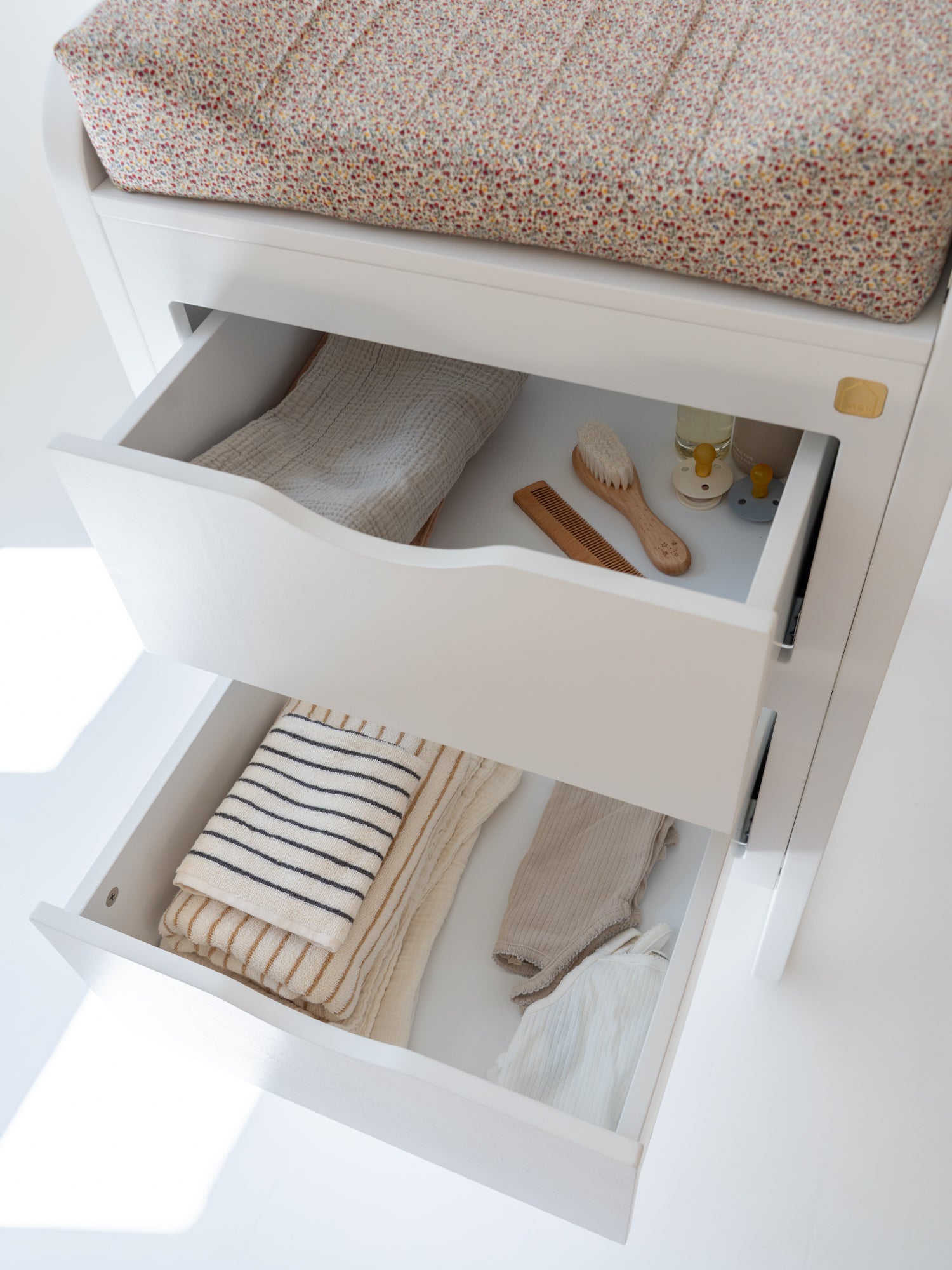 Open drawer with baby items including a seat cover, clothes, and a brush on a white background