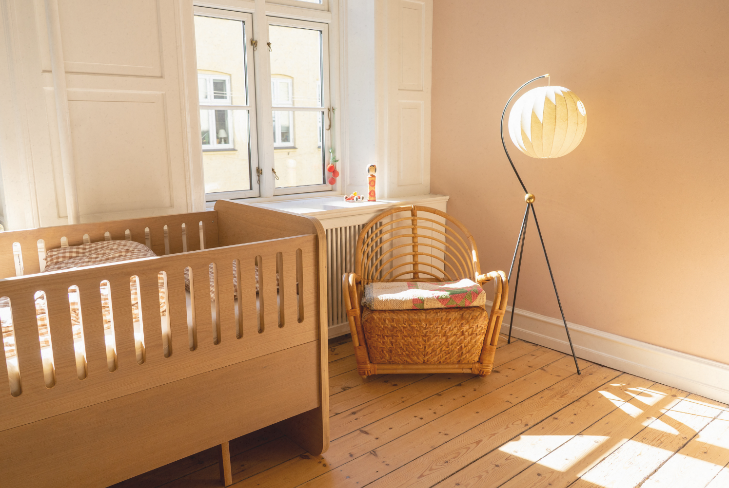 Nursery room with wooden crib, wicker chair, and floor lamp.