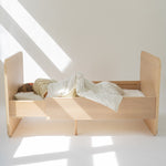 Wooden bed with a child sleeping in a well-lit room with a skylight.