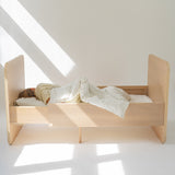 Wooden bed with a child sleeping in a well-lit room with a skylight.