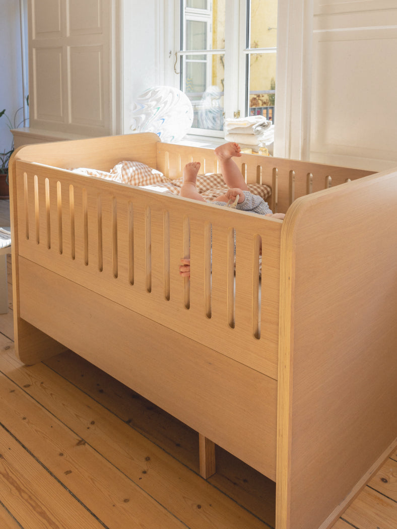Wooden crib with a baby inside in a well-lit room.