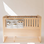 Wooden crib with a gray storage bag containing toys on a white background