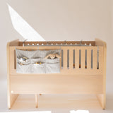 Wooden crib with a gray storage bag containing toys on a white background