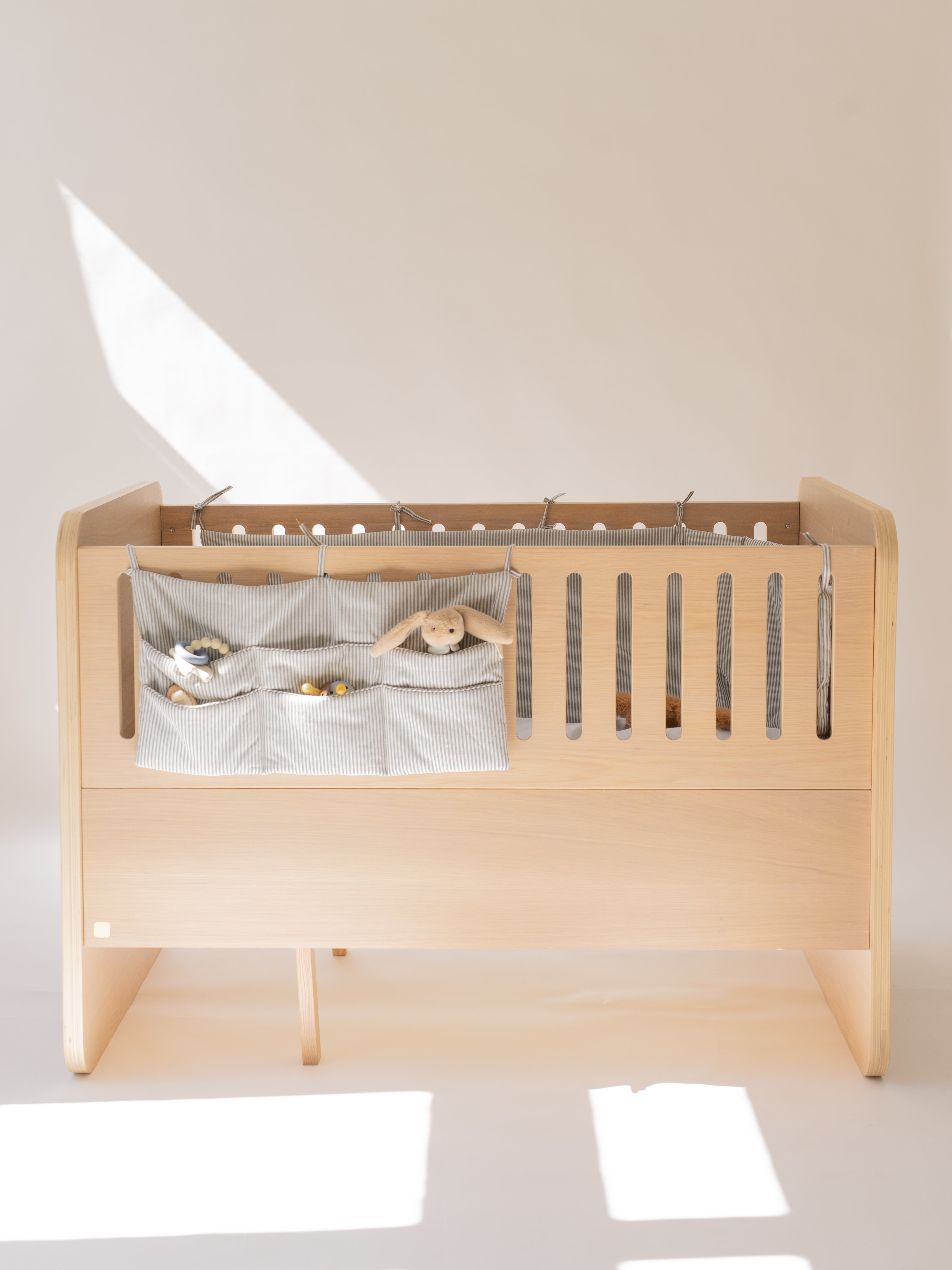 Wooden crib with a gray storage bag containing toys on a white background
