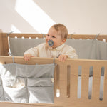 Baby in a crib with a pacifier, smiling in a bright room.