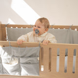 Baby in a crib with a pacifier, smiling in a bright room.