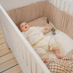 Baby in a crib with checkered bedding and toys