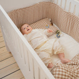 Baby in a crib with checkered bedding and toys