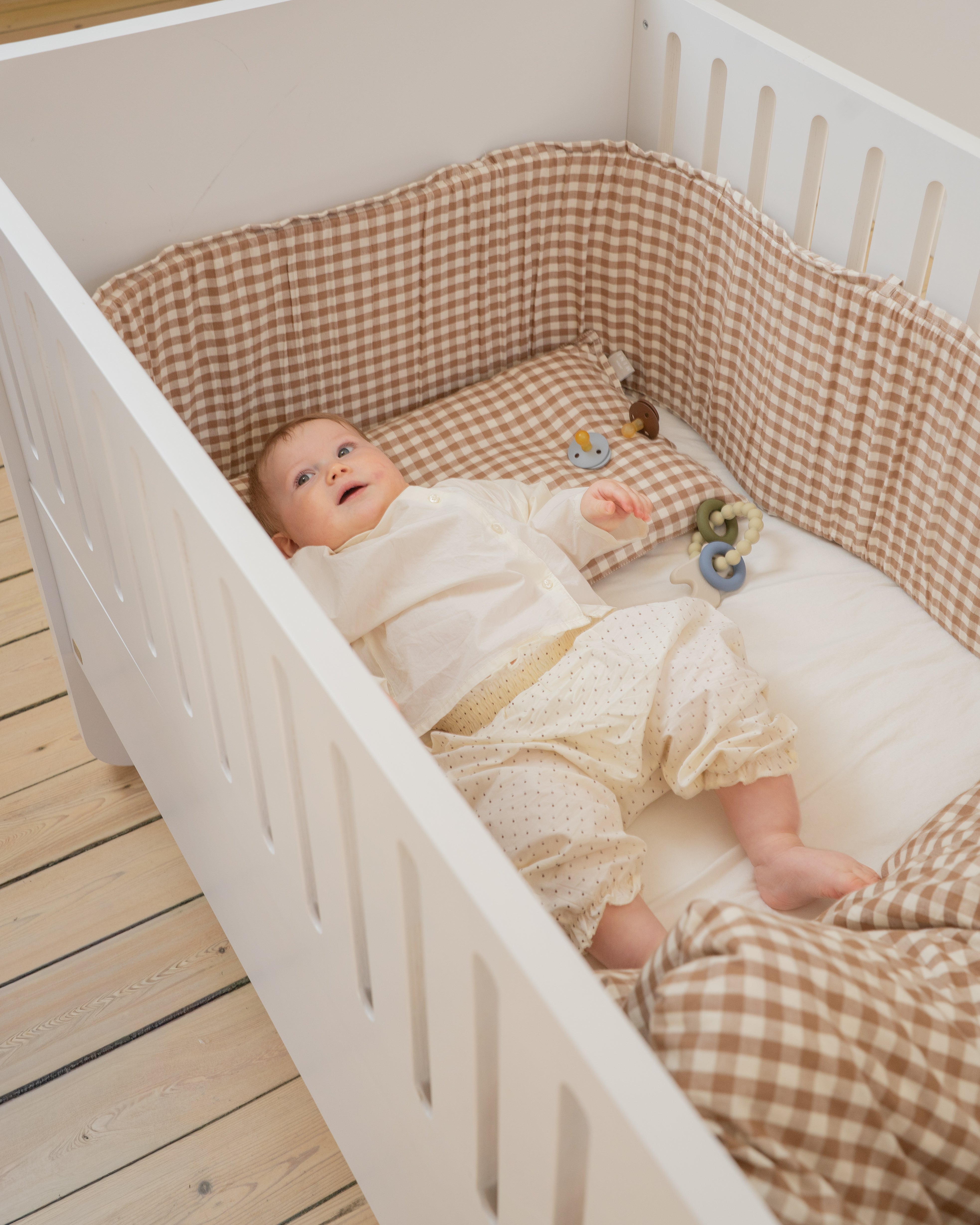 Baby in a crib with checkered bedding and toys