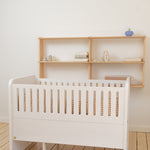 White crib with wooden slats and a wooden shelf unit in a minimalistic room.
