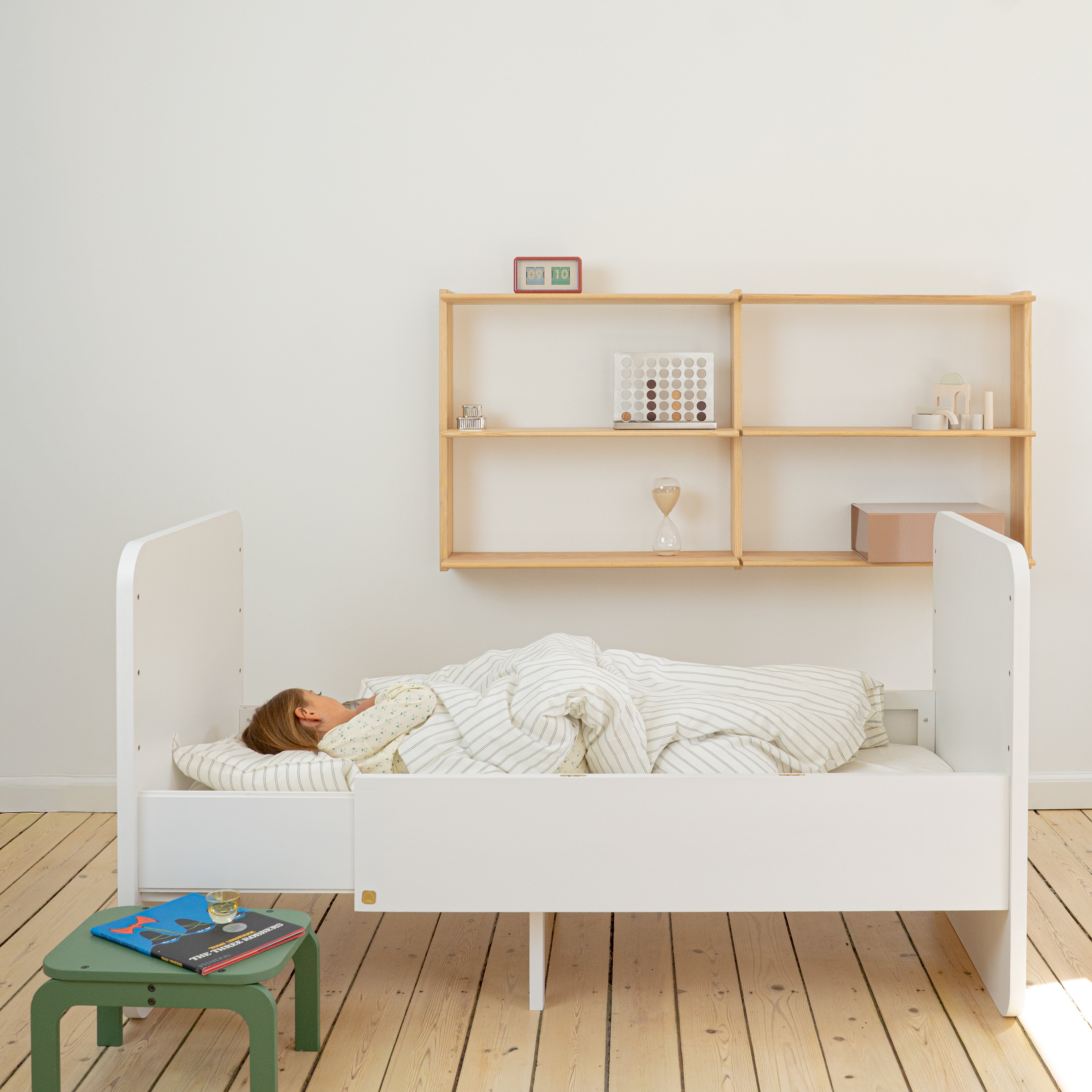 Person lying in a white bed with wooden shelves in the background