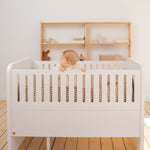 Baby in a white crib with wooden shelves in the background