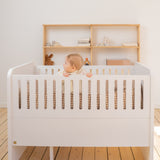 Baby in a white crib with wooden shelves in the background