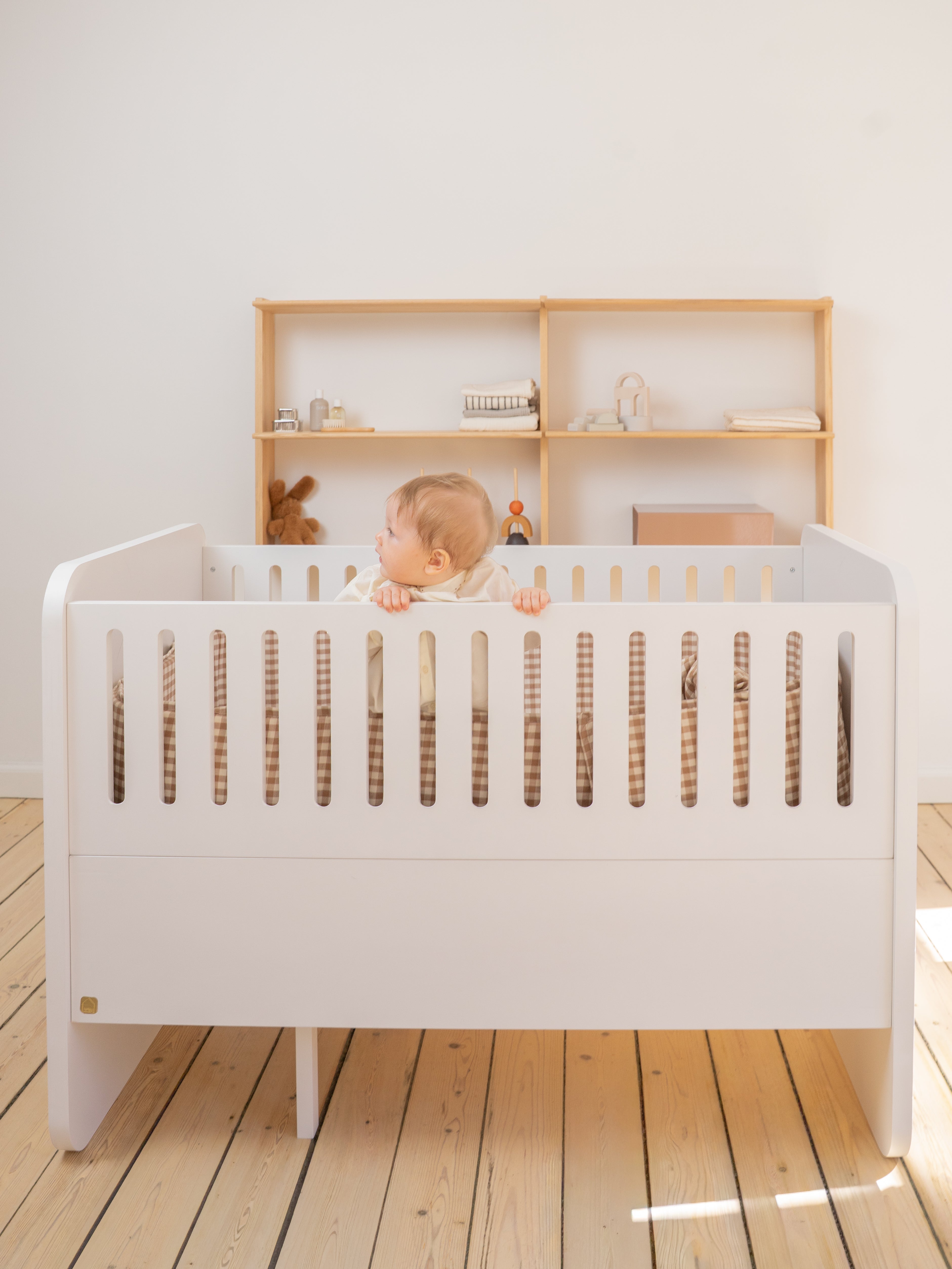 Baby in a white crib with wooden shelves in the background